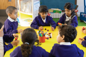 Olive School children in purple uniforms engaged in a hands-on learning activity with blocks at a classroom table
