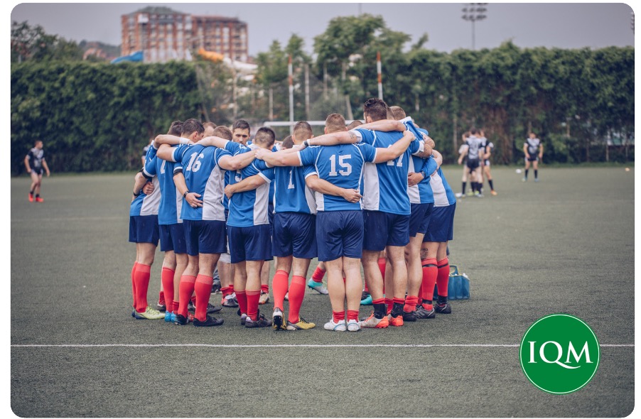 A football team discussing strategy in a match, with branded IQM logo