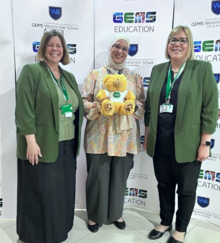 Two assessors and teachings standing together holding toy bear
