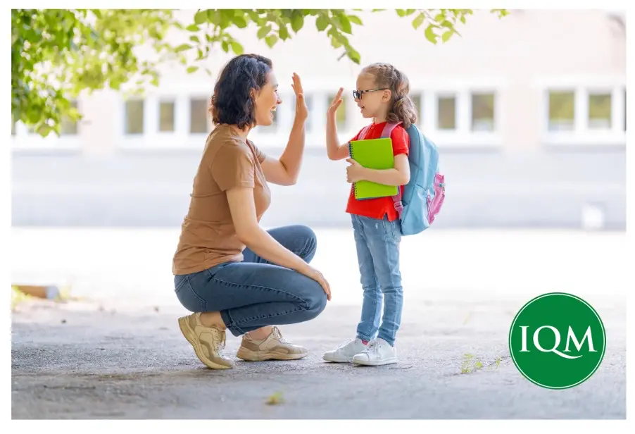 Teacher welcoming young girl in to school for the day with a high five