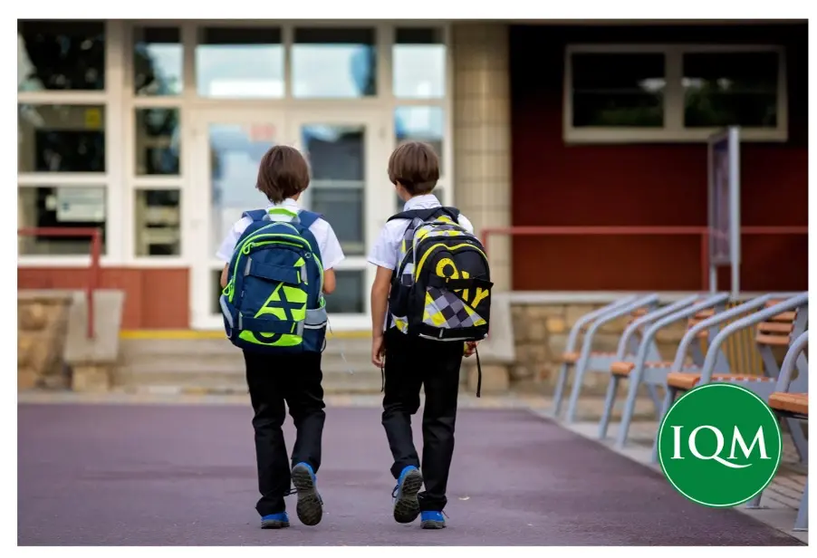 Two young boys with backpacks walking in to school together